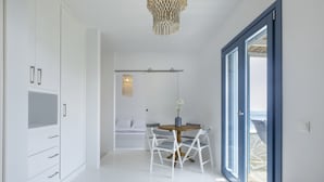 Un dormitorio moderno con cama, armario, zona de comedor con sillas y una mesa, y vista a través de una puerta.
