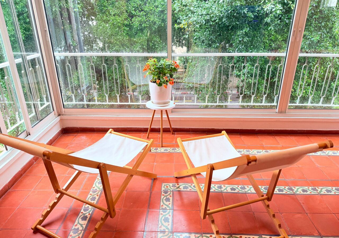 A balcony with two wooden chairs and a potted plant.