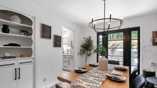 Uma sala de jantar moderna com mesa de madeira, cadeiras pretas e um candelabro.
