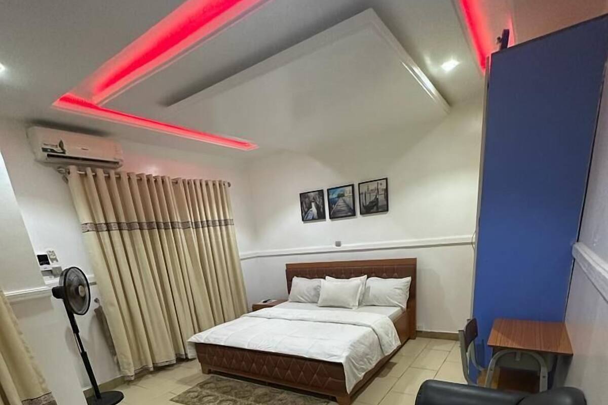 A bedroom with a bed, a desk, a chair, and a ceiling fan.
