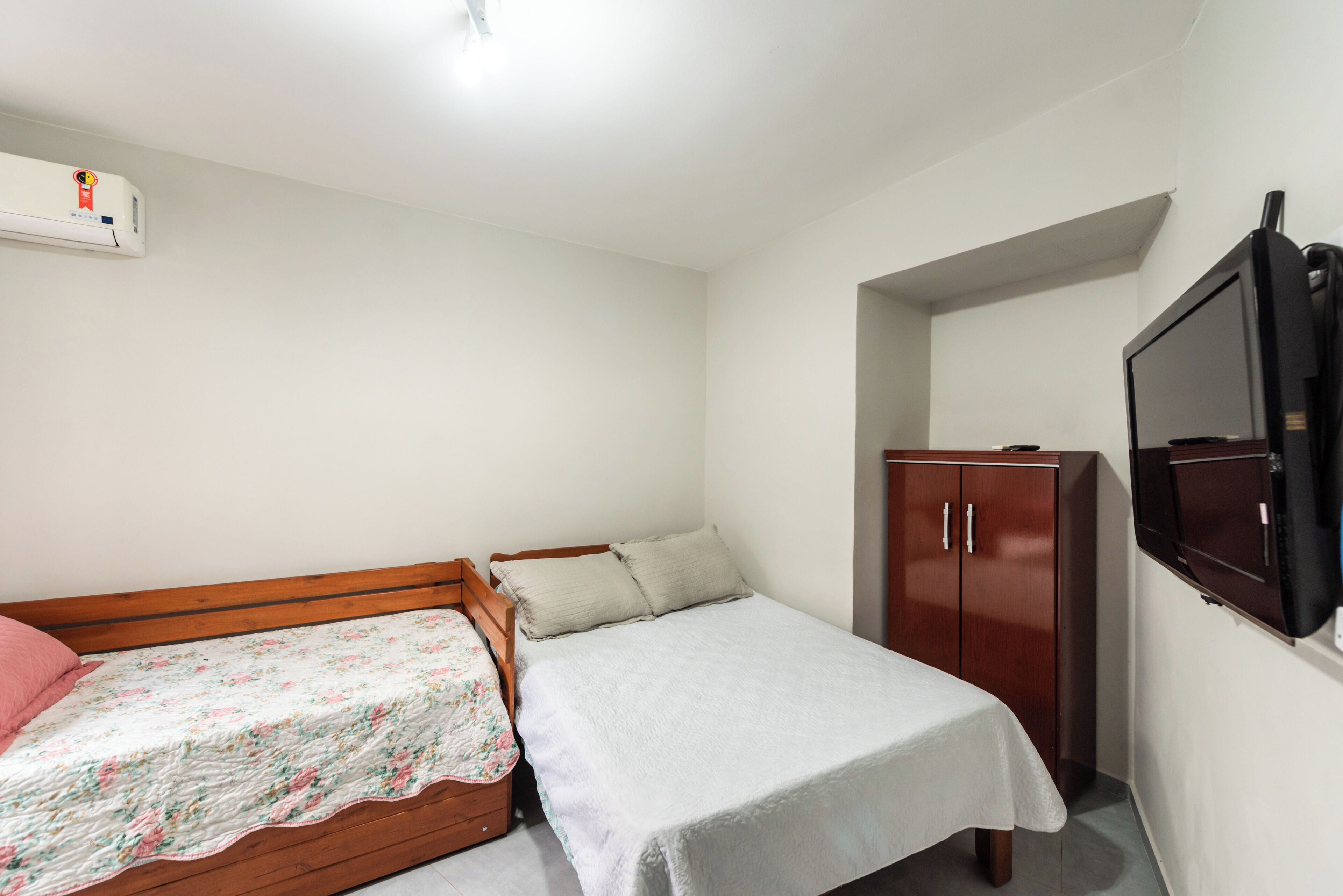 A bedroom with a wooden bed, a small bedside table, a wardrobe, and a television on the wall.