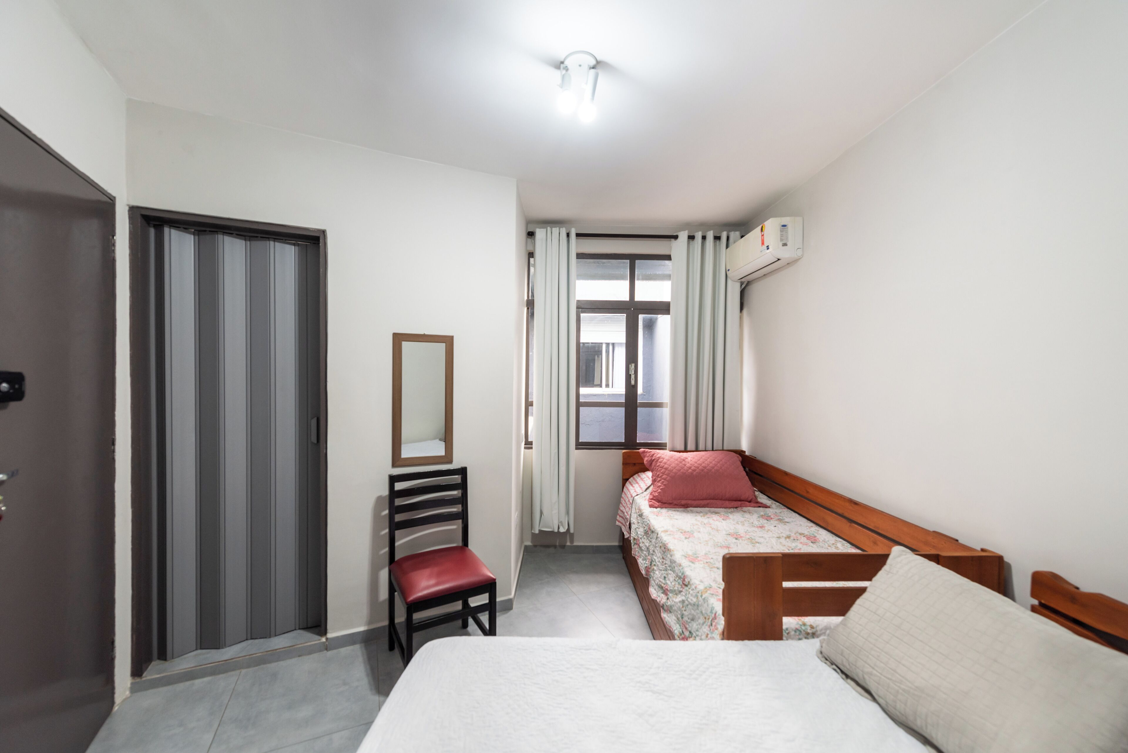 A bedroom with a bed, a chair, a mirror, and a window with curtains.