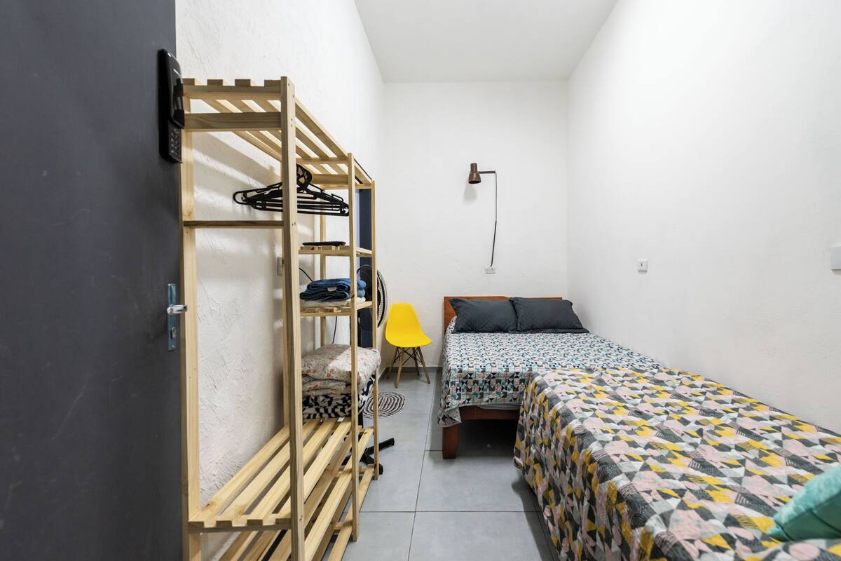 Una stanza piccola e luminosa con un letto a castello, un letto singolo, una scrivania e una sedia.