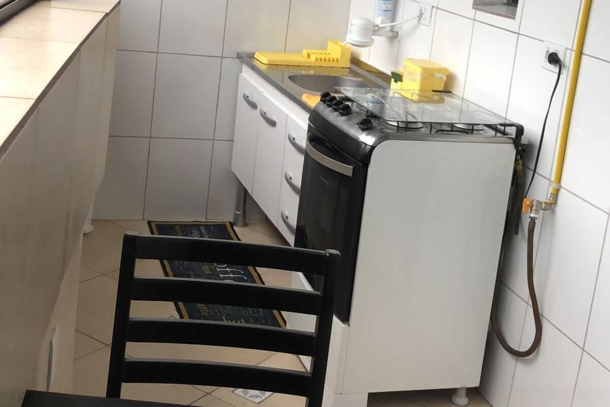Una cucina compatta con mobili bianchi, un lavandino e un piano cottura. In primo piano, una sedia e un tavolo.