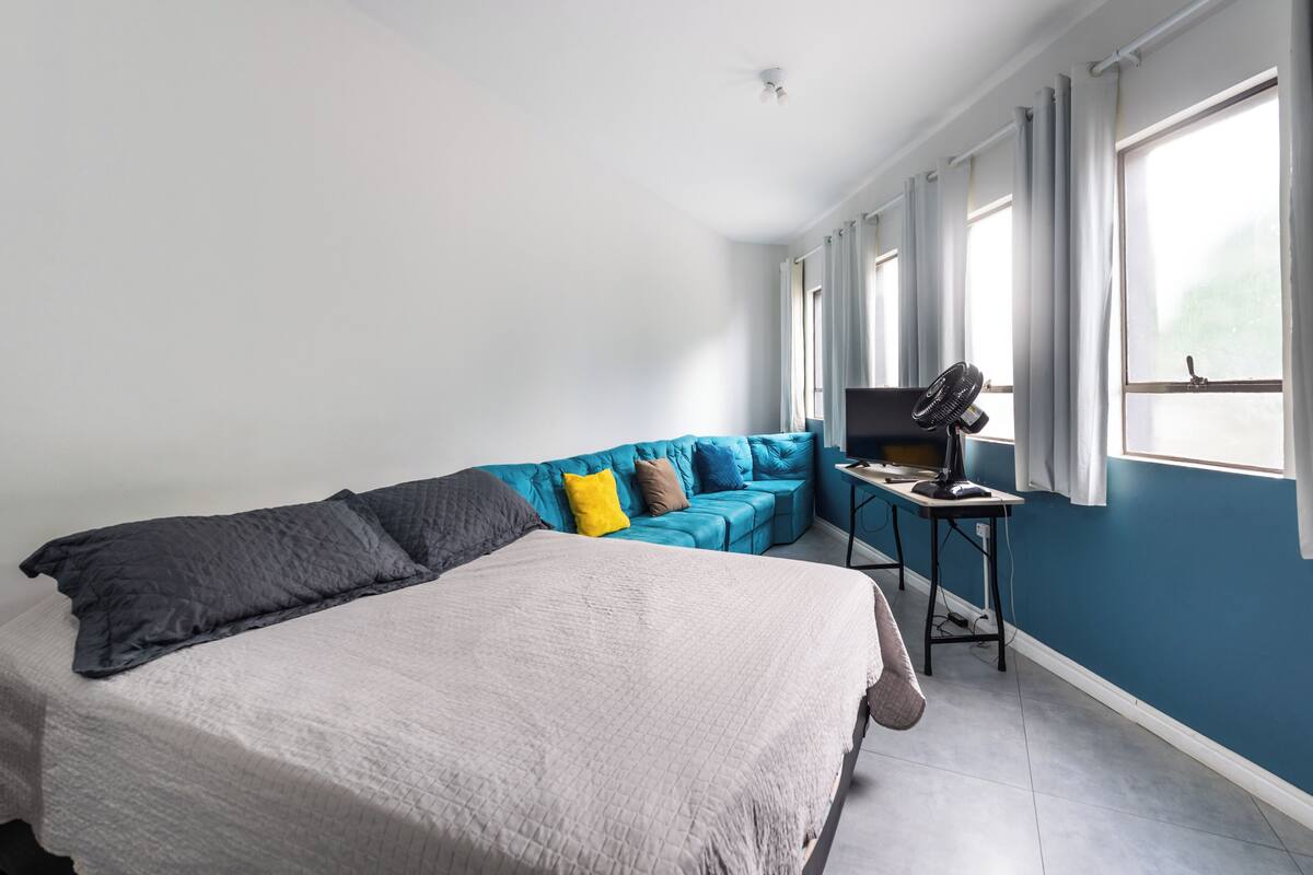 Una camera da letto con un letto, un divano blu, un tavolino con una sedia e una finestra con tende.