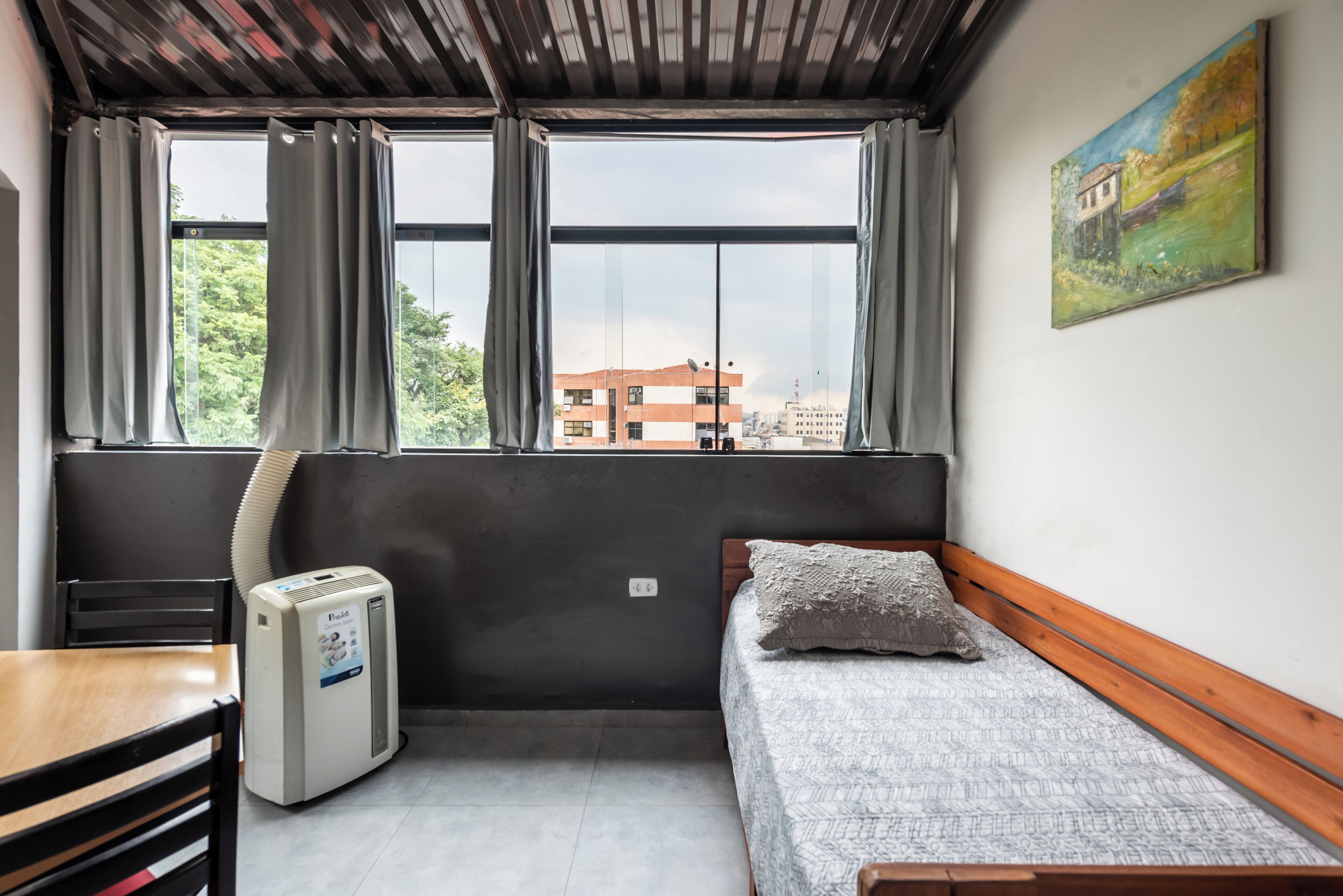 Una habitación pequeña con cama, una mesita, una silla, un calentador y una ventana con cortinas.
