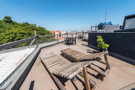 A rooftop terrace with wooden loungers, a table, and chairs.