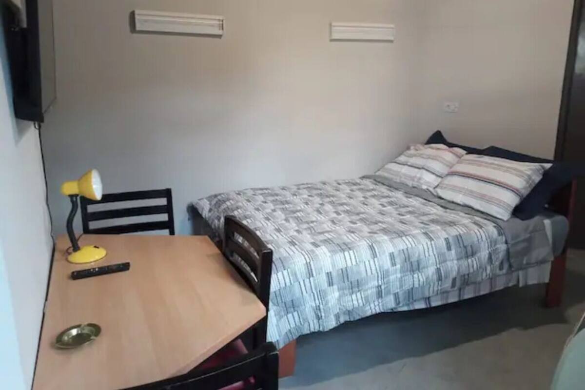 Una stanza piccola e arredata in modo essenziale, con un letto, una scrivania e una sedia.