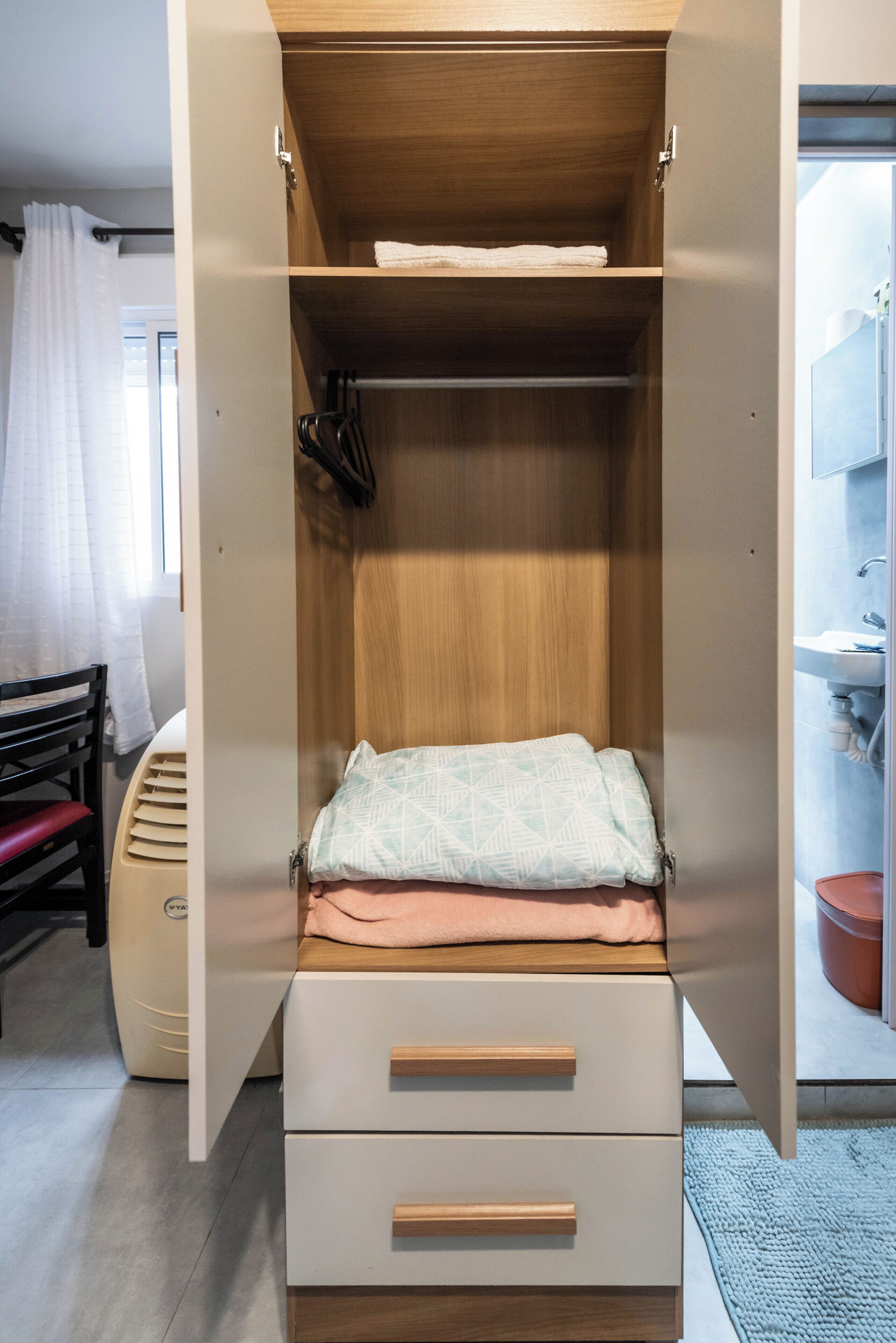 A bedroom with a wooden wardrobe, a bed with a patterned pillow, and a window with curtains.