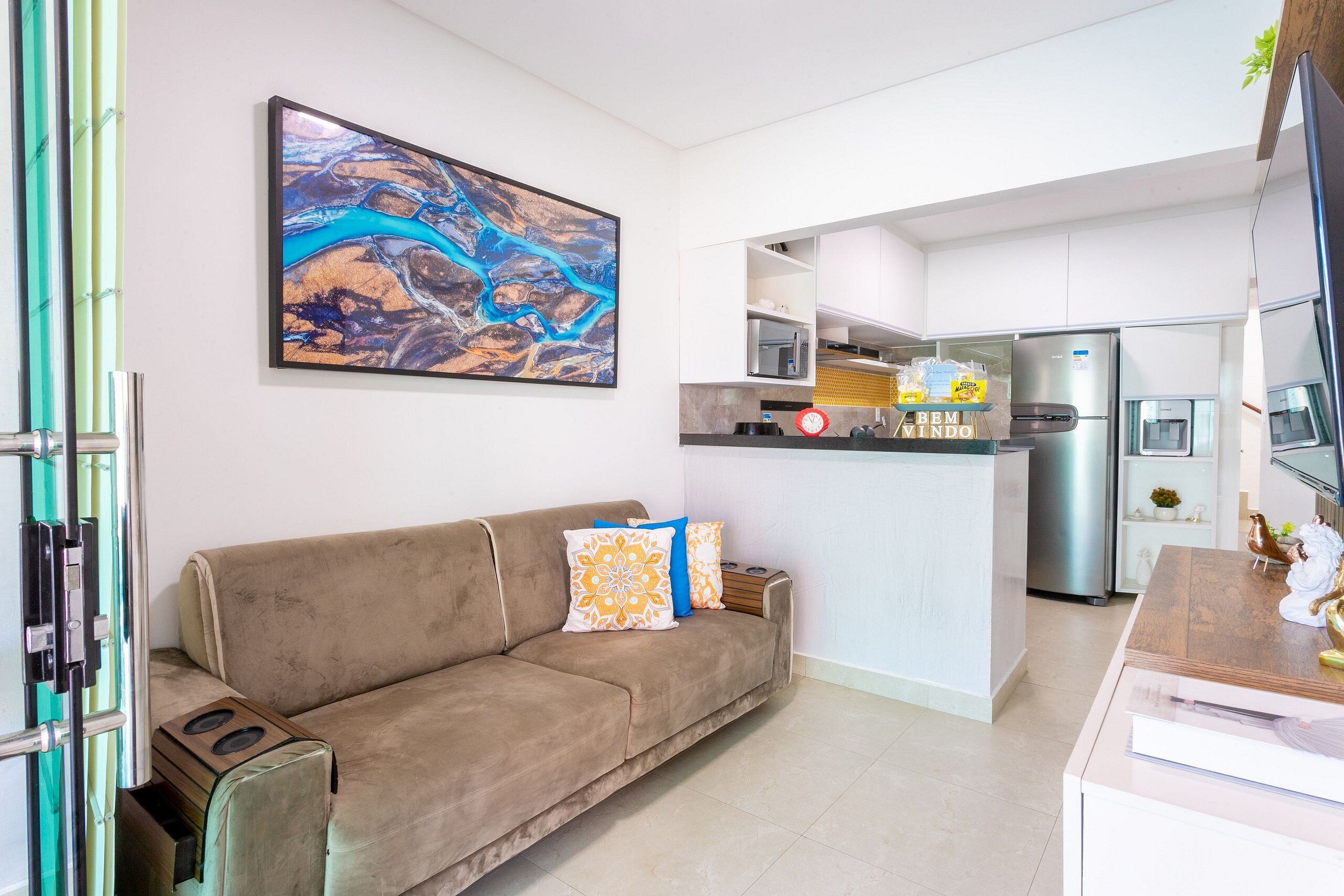 A modern living room with a sofa, a coffee table, and a kitchen area with a refrigerator, microwave, and sink.