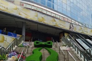 A modern building with a glass facade, a green sculpture on the staircase, and floral decorations. - Haolong Hotel (Qionghai Yinhai Road Grain Street Branch) (Qionghai)
