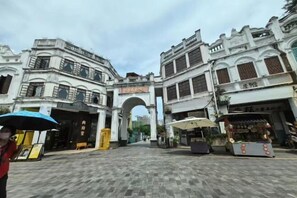 An urban street with historic buildings, a prominent archway, and a street vendor. - Haolong Hotel (Qionghai Yinhai Road Grain Street Branch) (Qionghai)