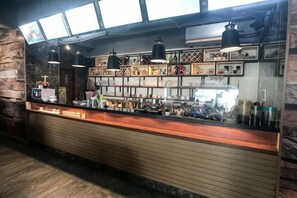 Een bar met een houten toonbank, hangende hanglampen en een bakstenen muur.