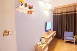 A modern living room with a flat-screen TV, a wooden coffee table, a blue armchair, and a shelf with decorative items. - Haolong Hotel (Qionghai Yinhai Road Grain Street Branch) (Qionghai)