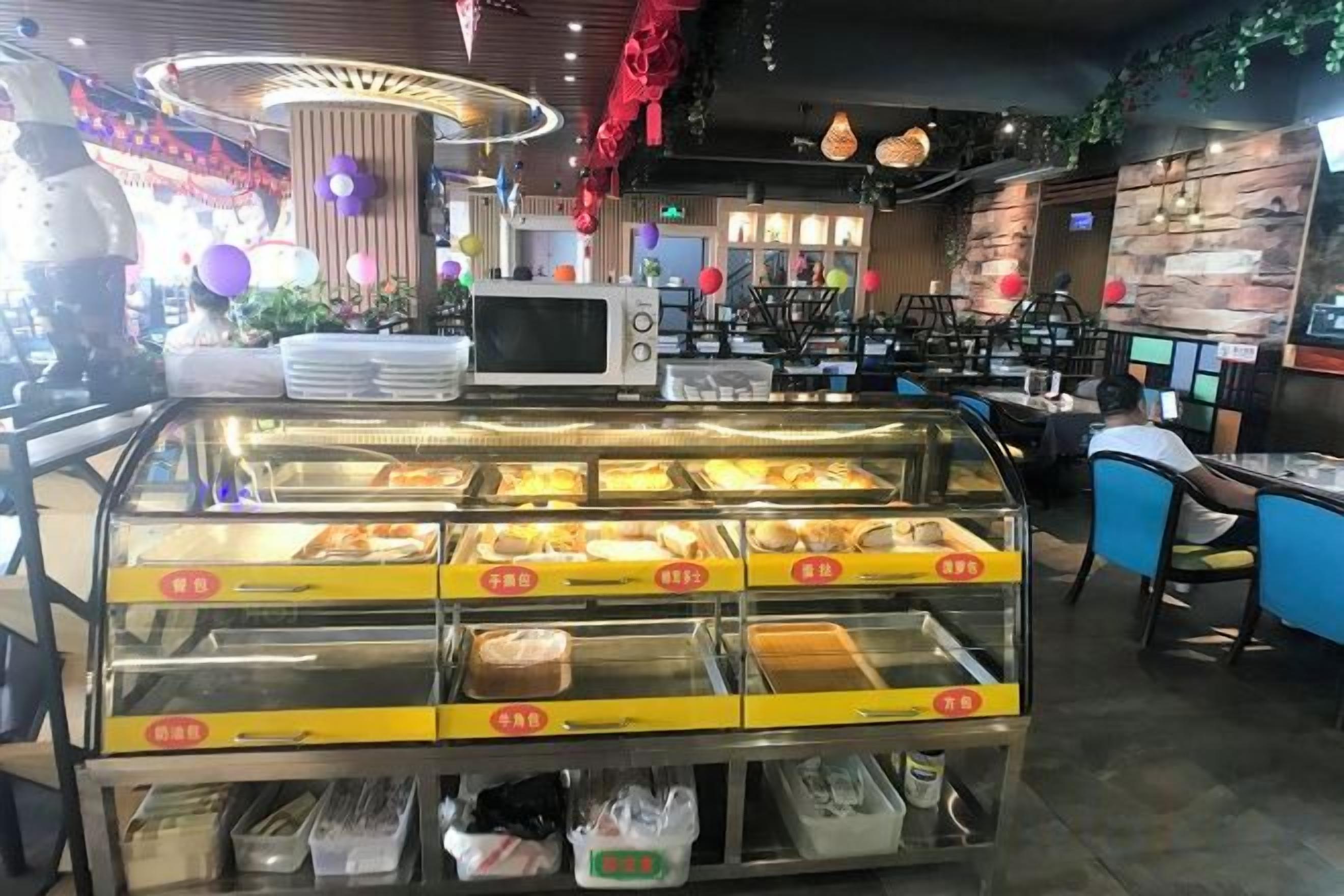 Mostrador de panadería con diversos productos horneados, un microondas y zonas de estar en un restaurante.