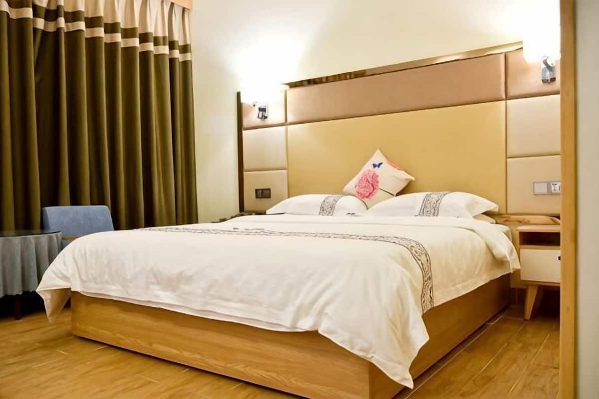 A hotel room with a large bed, wooden headboard, bedside tables, and a curtain.