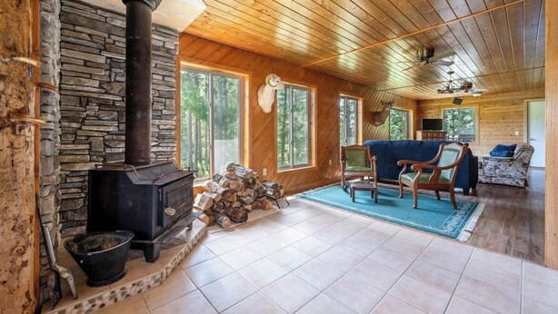 A log cabin interior with a stone fireplace, wooden walls, and a stone chimney.