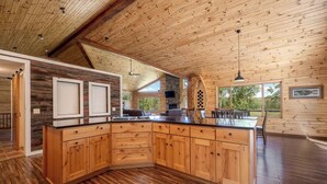 A spacious kitchen with a large island, wooden cabinetry, and a stone fireplace.