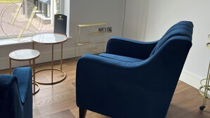 A modern room with a blue armchair, a small round table, and a tall floor lamp. A large window offers a view of a house and a lake. - Luxury Home on Valentia Island, Nightstown with sea view, Electric Car Charger (Valentia Island)