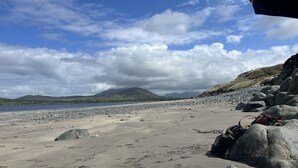 A beach with large rocks, a sandy shore, and a mountain in the distance. - Luxury Home on Valentia Island, Nightstown with sea view, Electric Car Charger (Valentia Island)