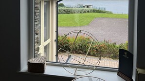 A window with a view of a lake, a grassy area, and a building across the water. - Luxury Home on Valentia Island, Nightstown with sea view, Electric Car Charger (Valentia Island)