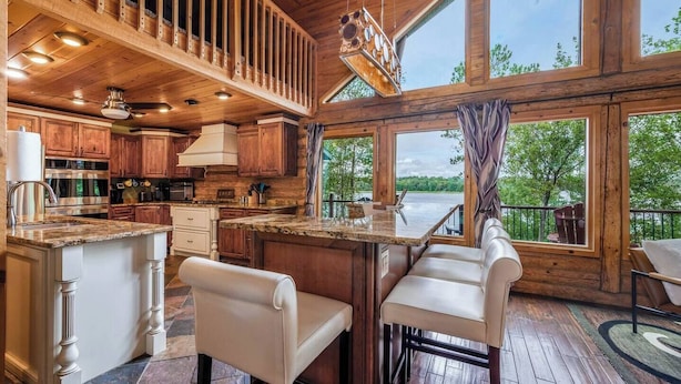 A spacious kitchen with a large island, wooden cabinetry, and a view of a lake. - The Hideaway on Little Jay | Log Home | (Cohasset)