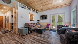 A spacious living area with a wooden ceiling, a large clock, and a television. - Dog Friendly, Cozy, Private, Convenient | Long Lake Lookout (Cohasset)