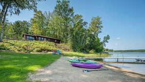 A lakeside property with a wooden cabin, kayaks, and a gravel path leading to the water.