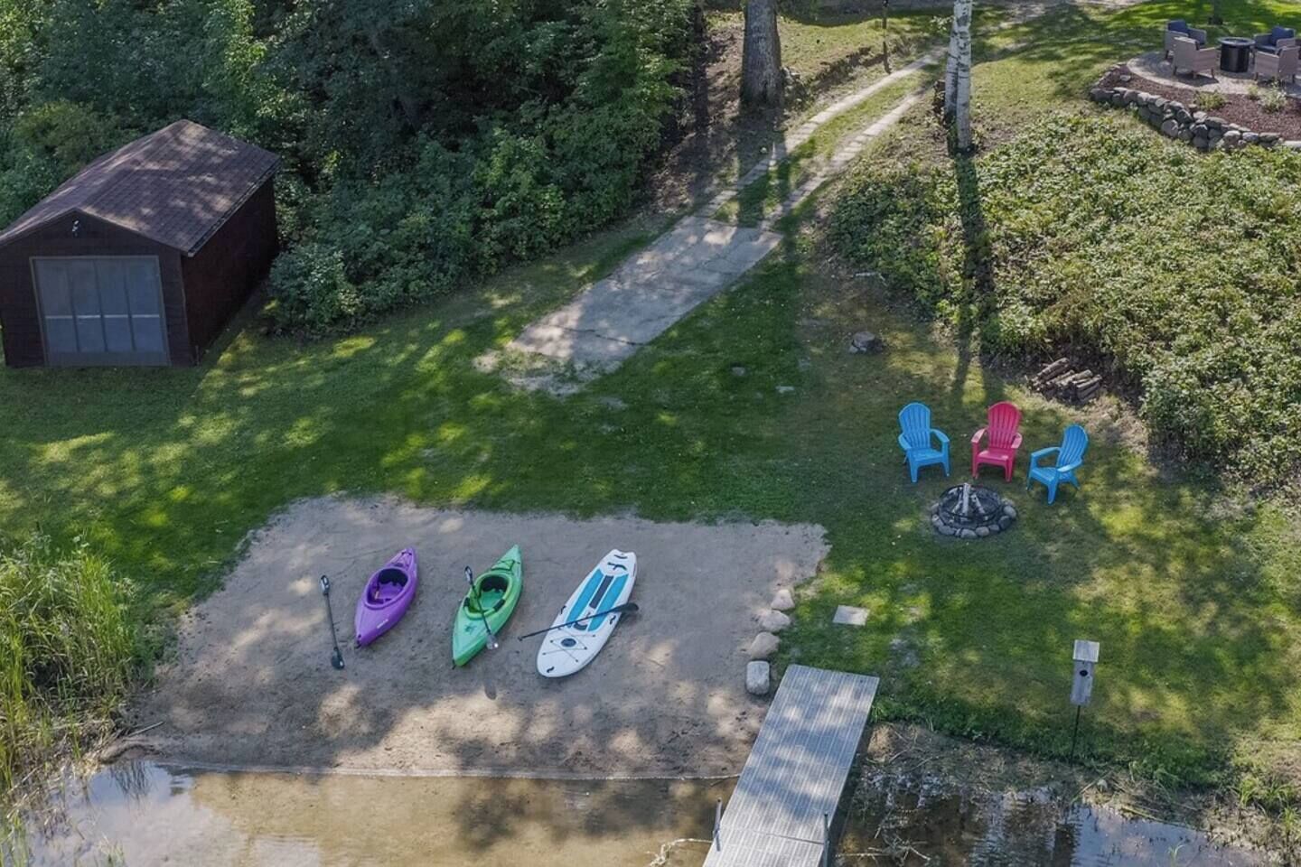 Un espacio al aire libre con césped, kayaks, sillas y un cobertizo.