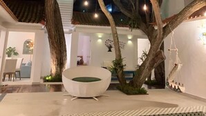 Un árbol con luces colgantes, una zona de estar exterior blanca y una piscina.