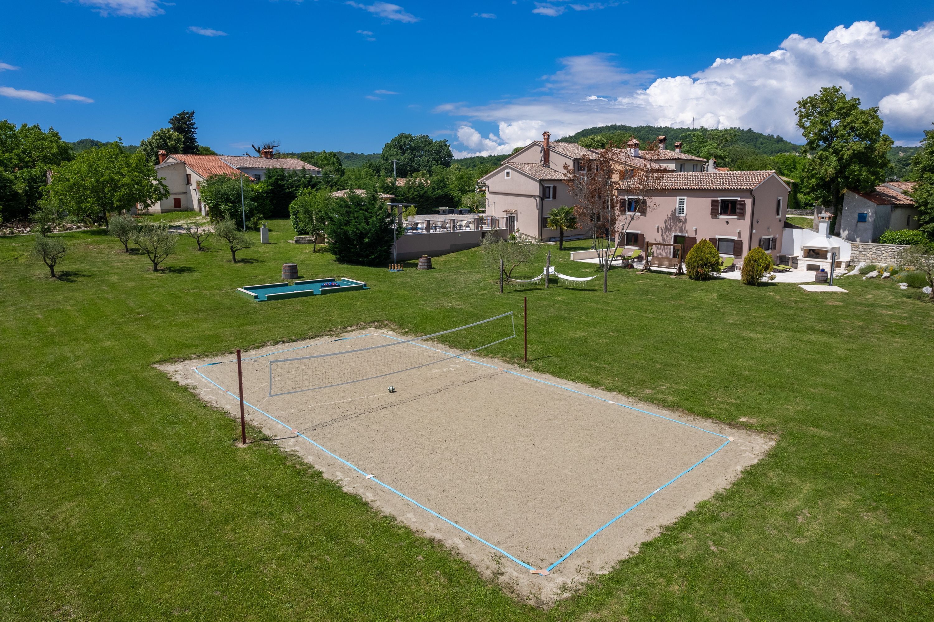 A tennis court surrounded by a grassy area with a pool and houses in the background.