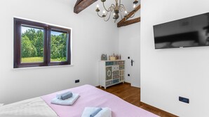 A bedroom with a bed, a chandelier, a television, a dresser, and a window with a view of greenery. - Vesna Branka in Pi an (Pican)