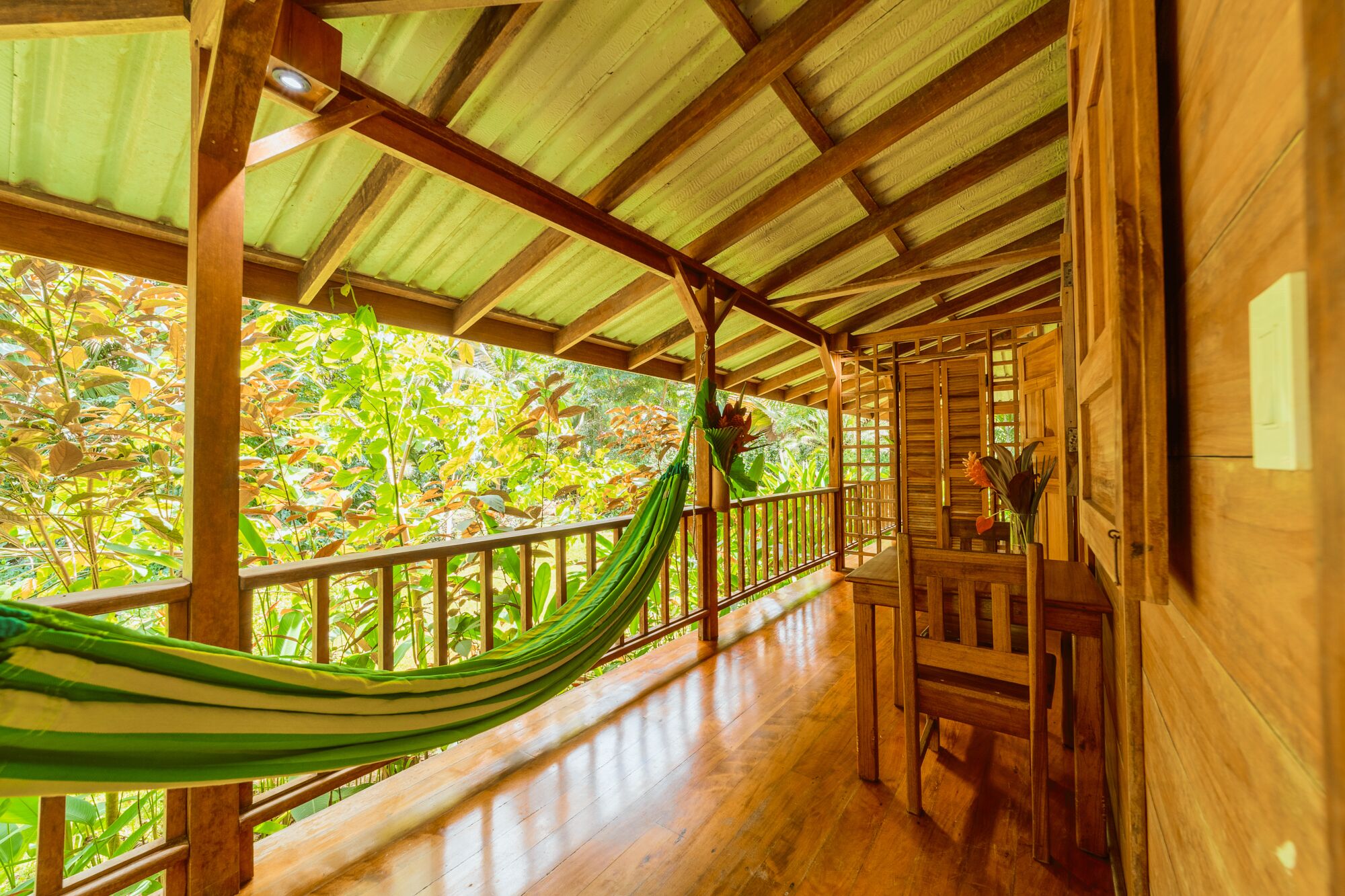 A wooden porch with a hammock, wooden railing, and a view of lush greenery.