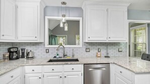 A kitchen with white cabinets, a stainless steel dishwasher, a double sink, and a hanging light fixture.