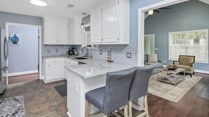 A modern kitchen with white cabinets, a marble island, and a gray bar stool.