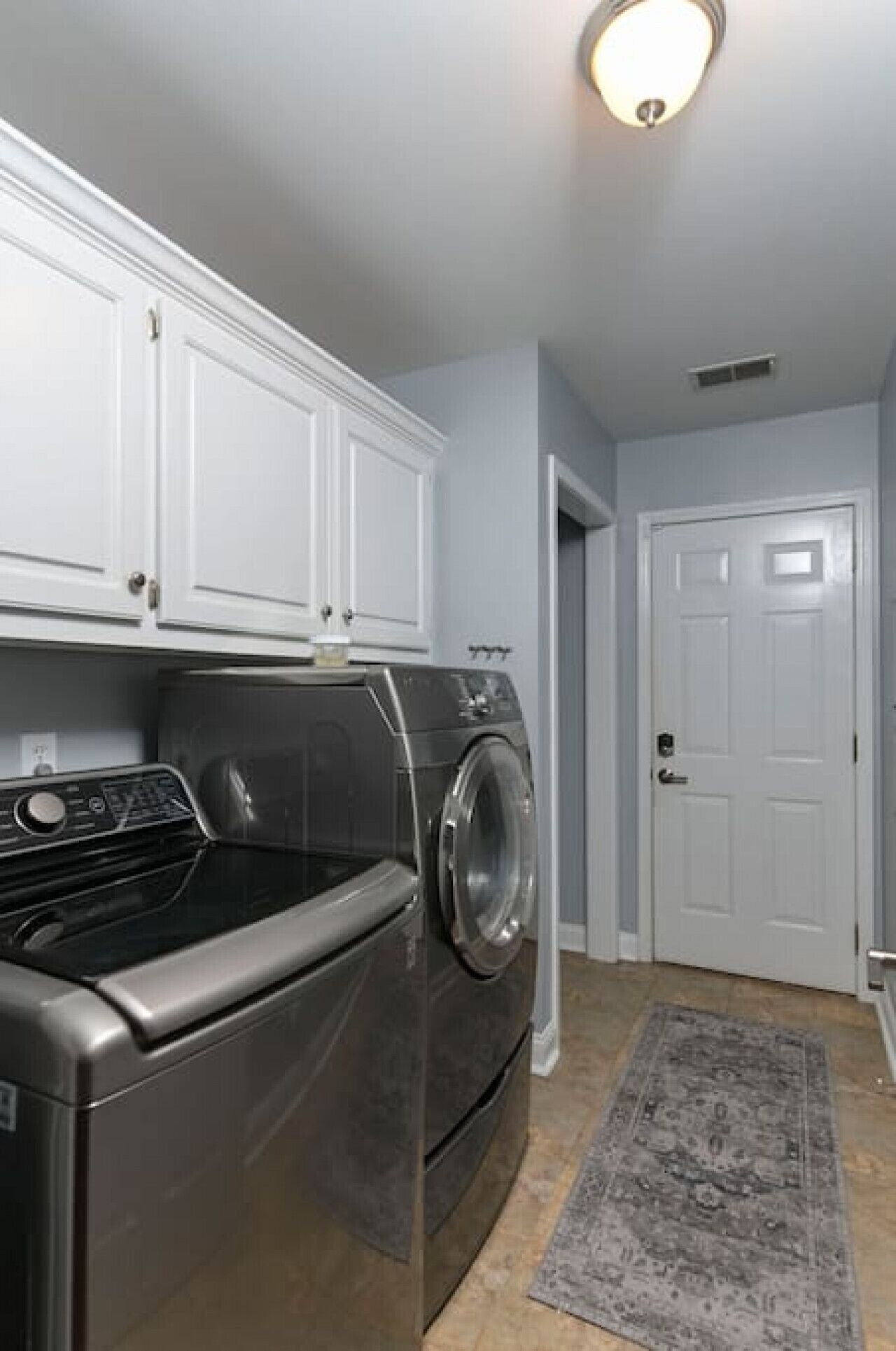 A laundry room with a stainless steel washer and dryer, white cabinets, and a gray rug.
