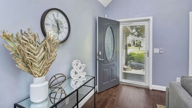 A modern living room with a grey door, a wall clock, and decorative items.