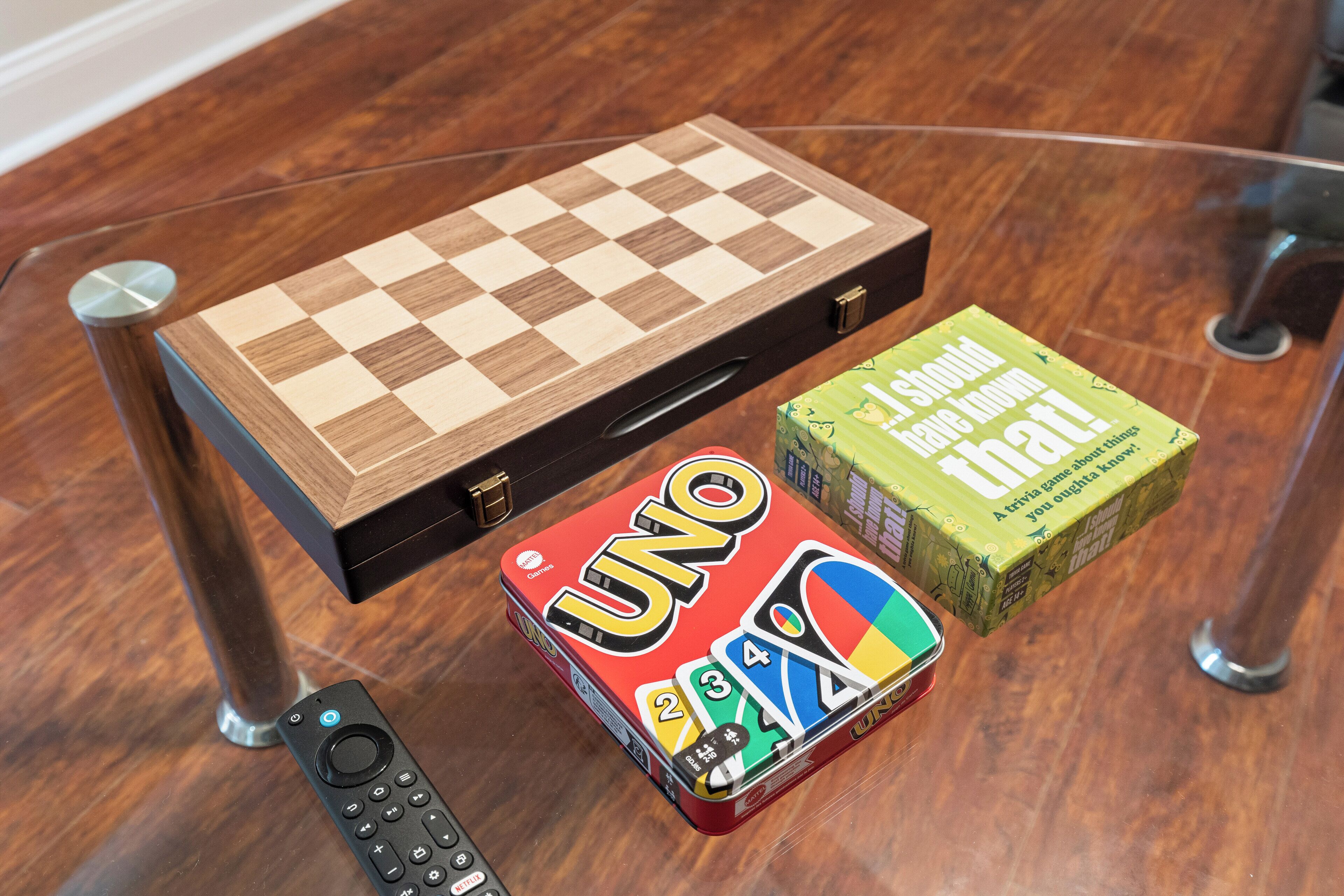 Um jogo de tabuleiro de madeira, uma caixa de UNO e um controle remoto sobre uma mesa de vidro.