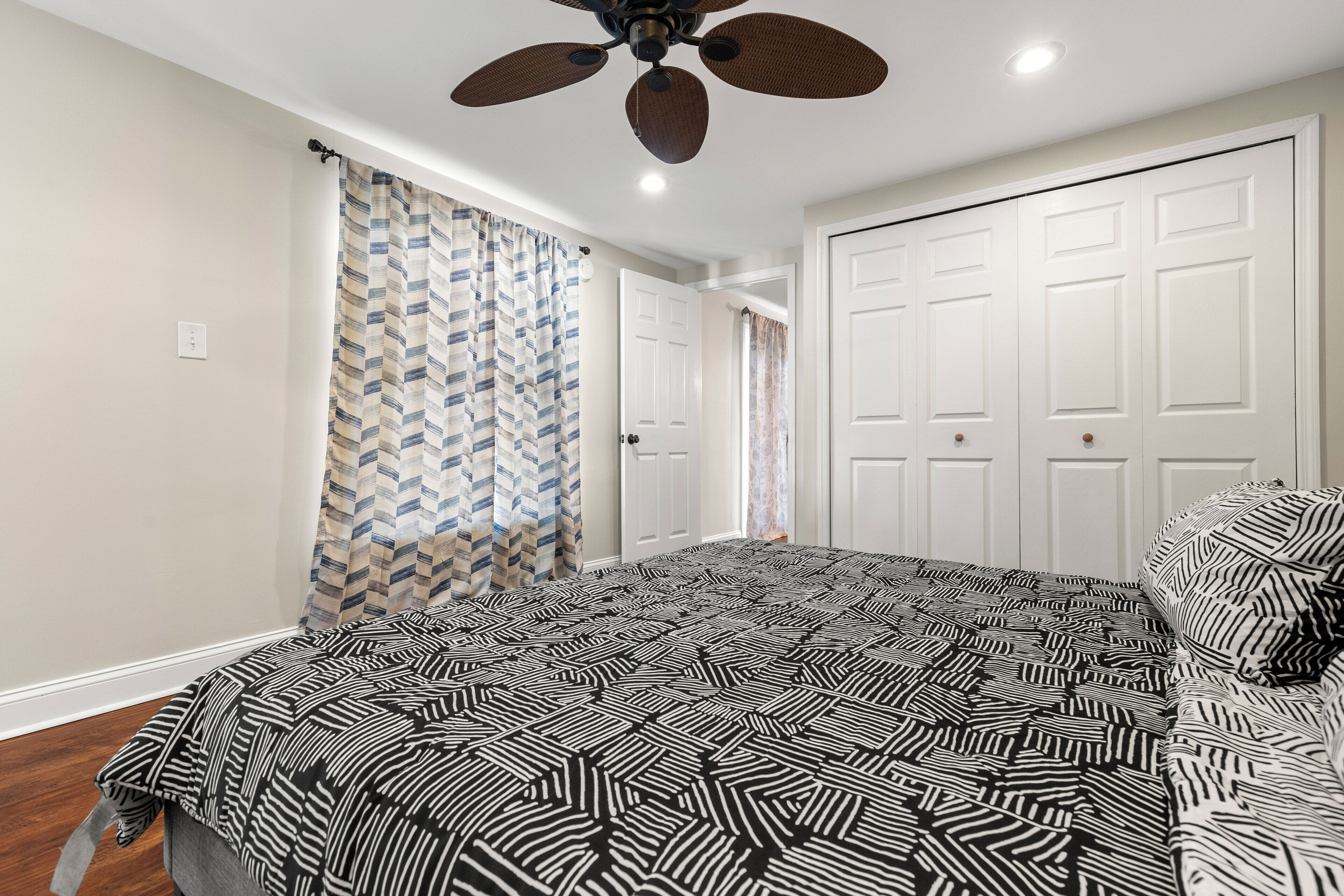 A bedroom with a patterned bedspread, a ceiling fan, and white doors.