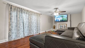 Ein Wohnzimmer mit einem dunkelbraunen Ledersofa, einem Glastisch und einem flachbildfernseher, der an der Wand befestigt ist.