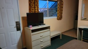 A room with a television on a wooden cabinet, a window with curtains, a door, and a small desk with a chair. - Copa Budget Inn (Medicine Lodge)