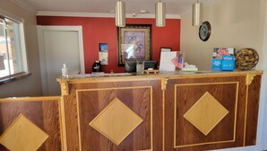A reception desk with a wooden finish and diamond-shaped panels, a framed picture on the wall, and a clock above it. - Copa Budget Inn (Medicine Lodge)