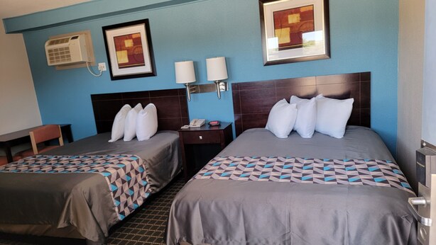 A hotel room with two beds, a nightstand, a lamp, and a framed picture on the wall. - Copa Budget Inn (Medicine Lodge)