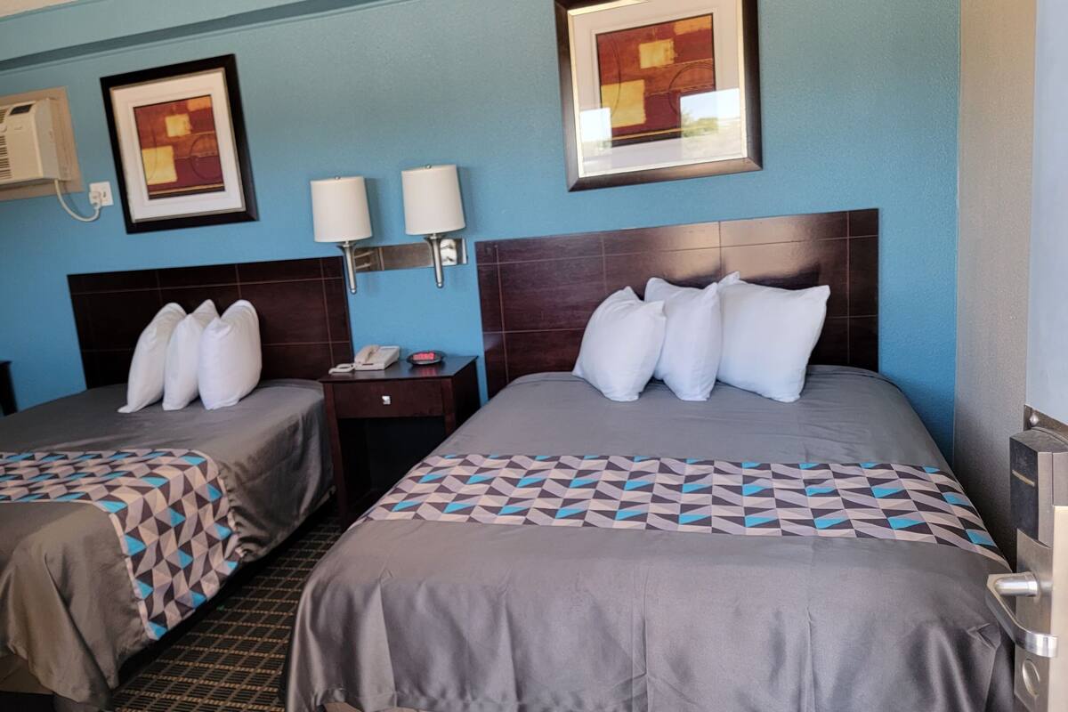 A hotel room with two beds, a nightstand, a lamp, and a framed picture on the wall.