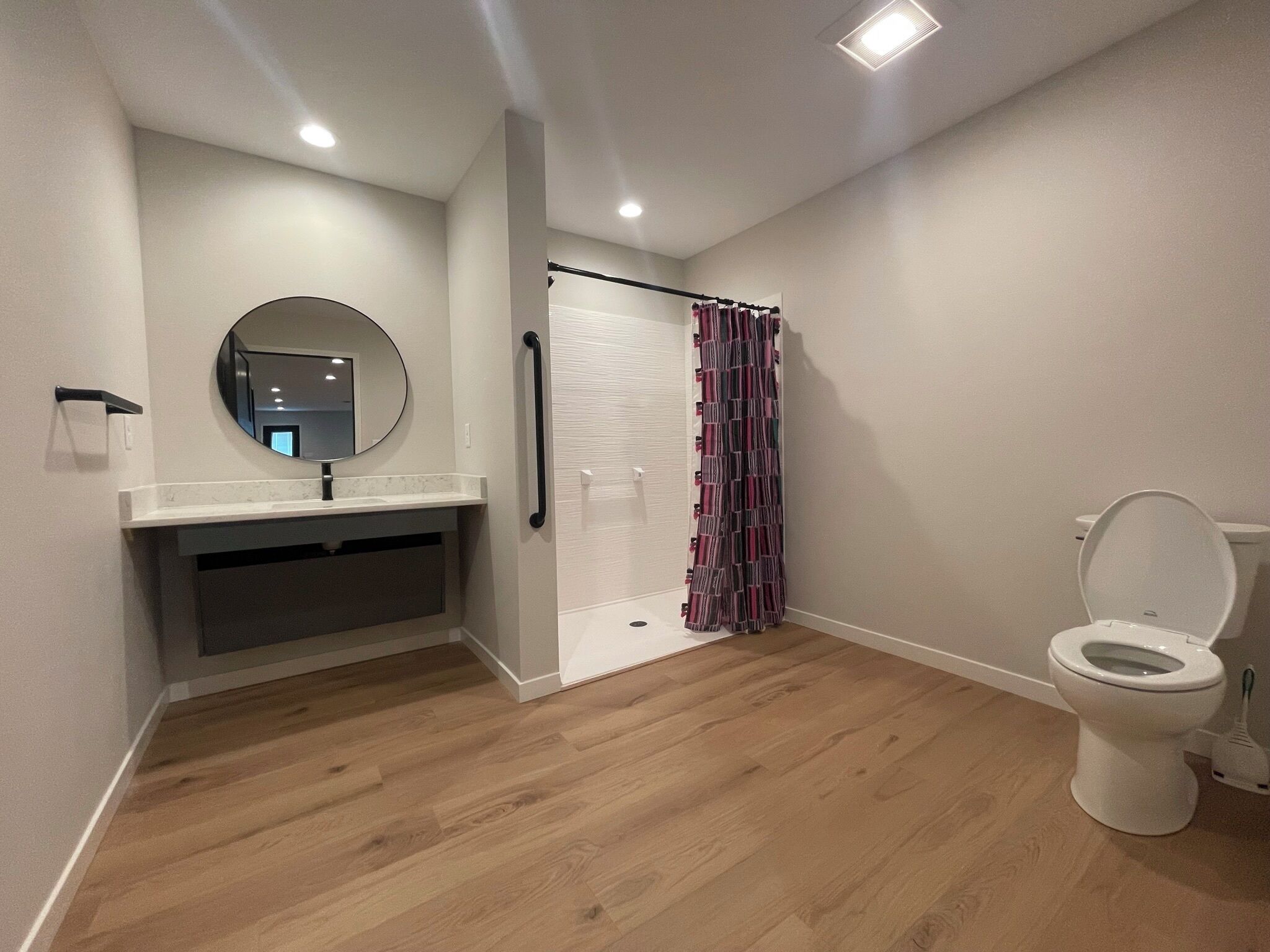 Une salle de bain avec un plancher en bois, des toilettes blanches, un lavabo avec un miroir et un rideau de douche.