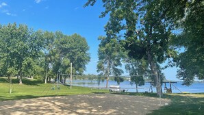 A sandy volleyball court with a net, surrounded by trees and a lake view. - Guest House at Geneva Beach Resort - Views of Lake Geneva (Alexandria)