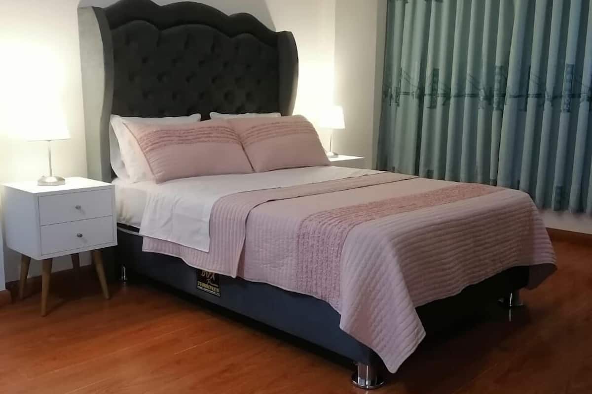 A neatly made bed with a tufted headboard, two bedside tables with lamps, and a large window with curtains.