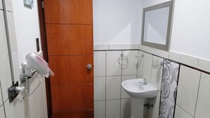 A bathroom with a wooden door, white tiles, a sink, a toilet, and a mirror. - Zona céntrica Lima Histórica (Lima)