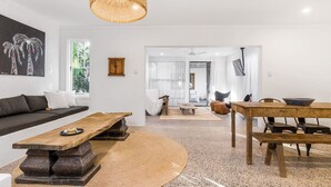 Un salon moderne avec un canapé, une table basse et une table à manger. Une grande fenêtre offre une vue sur la verdure environnante.