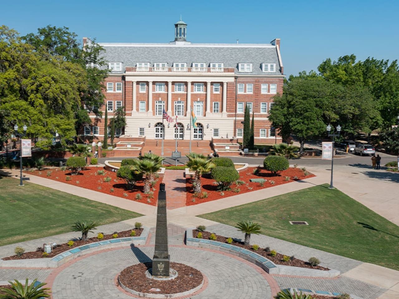 A large brick building with a central courtyard and a tall monument.